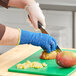 A person wearing blue Ansell medium-duty gloves peeling a mango.