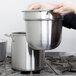 A hand holding a Vollrath stainless steel pot over a stove.