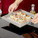 A person holding a Vollrath stainless steel square serving tray of sushi.