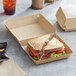 A Sabert corrugated kraft take-out box with a sandwich inside and a cup of brown liquid with ice on the side.