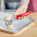 A person using a red Choice #24 ergonomic thumb press ice cream scoop to serve a ball of food.