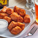 A plate of Stone Gate Buffalo Chicken Tater Kegs with a bowl of white sauce and a fork on a table.