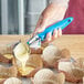 A person using a blue handled Choice 16 thumb press to pour batter into cupcakes.