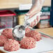 A person using a white Choice thumb press scoop to make meatballs.