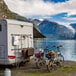 A white RV parked next to a lake with a bicycle on the back.