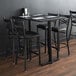 A Lancaster Table & Seating black cast iron bar height end column table base with chairs and menus.
