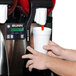 A person using a Bunn Ultra-2 slushy machine to pour a drink into a white cup with a red straw.
