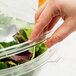 A hand putting a clear plastic dome lid on a bowl of salad.