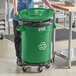 A woman in a green shirt standing next to a large green Lavex recycling can.