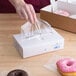 A hand putting LK Packaging plastic deli wrap on a box of donuts.