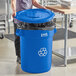 A woman standing in a school kitchen next to a blue Lavex recycling can with a blue lid.