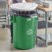 A woman standing next to a Lavex green recycling can with a white lid.