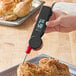 A hand using a Taylor digital folding thermometer to check the temperature of a chicken.
