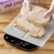 A gloved hand weighing food on a Taylor digital portion scale.