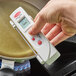 A hand holding a Cooper-Atkins digital infrared thermometer over a pan.