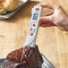 A hand using a Cooper-Atkins infrared thermometer to check the temperature of meat.