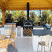 A Chicago Brick Oven wood-fired countertop pizza oven on a wood table in a large outdoor kitchen.