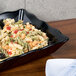 A black rectangular melamine tray with a bowl of pasta, olives, and peppers.
