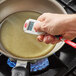 A hand holding a Cooper-Atkins digital infrared mini thermometer over a pan of liquid.