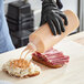 A person in black gloves using a Vollrath Twin Tip Squeeze Bottle to pour sauce on a sandwich.