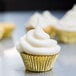 A close up of a cupcake with white frosting in a gold Ateco baking cup.