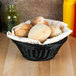 A black round polyweave basket filled with bread and rolls on a table.