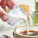 A hand pouring milk into a clear plastic Choice creamer cup.
