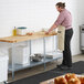 A man in a professional kitchen rolling out pizza dough on a Regency wood top work table with a galvanized base.