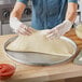 A person wearing gloves making a pizza on a Choice aluminum pizza pan.