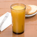A close-up of a light amber Cambro plastic tumbler filled with orange juice next to a plate of bread.