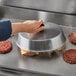A hand using a Choice aluminum basting cover to cook hamburgers on a grill.