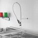 A Regency wall-mounted pre-rinse faucet with a hose attached to it above a stainless steel sink.
