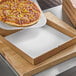 A pizza being cut into slices in a Choice Single Face Corrugated Pizza Pad box.