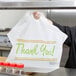 A woman holding a white LK Packaging plastic "Thank You" take-out bag.