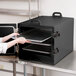A woman opening a black Cambro tray in a professional kitchen.
