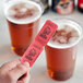 A hand holding a red 1-part "Beer" raffle ticket in front of two glasses of beer.
