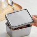 A hand opening a Matfer Bourgeat stainless steel mini container lid.