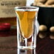 A Libbey tall shot glass filled with brown liquid on a table in a bar.