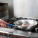 A hand cooking meat in a Vollrath aluminum fry pan with a blue handle.