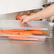 A person using a Carlisle clear plastic lid to cover a container of carrots.