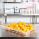 A Carlisle clear plastic food storage container on a table filled with oranges.