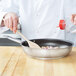 A chef stirring food in a Vollrath Centurion stainless steel fry pan with a wooden spoon.