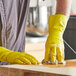 A person wearing a yellow Lavex latex glove cleaning a wooden surface.