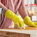 A person wearing yellow Lavex latex rubber gloves cleaning a wooden surface.