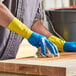 A man wearing blue and yellow Lavex dishwashing gloves cleaning a wooden surface.