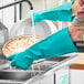 A person in a green Lavex nitrile glove washing dishes under a faucet.