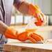 A man wearing orange Lavex neoprene/latex gloves cleaning a cutting board.