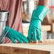 A person wearing Lavex green rubber dishwashing gloves cleaning a wood surface.