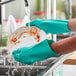A person wearing Lavex green nitrile gloves washing a plate under running water.