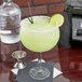 A Libbey Magna Grande Margarita glass with a drink and a lime wedge on a table.